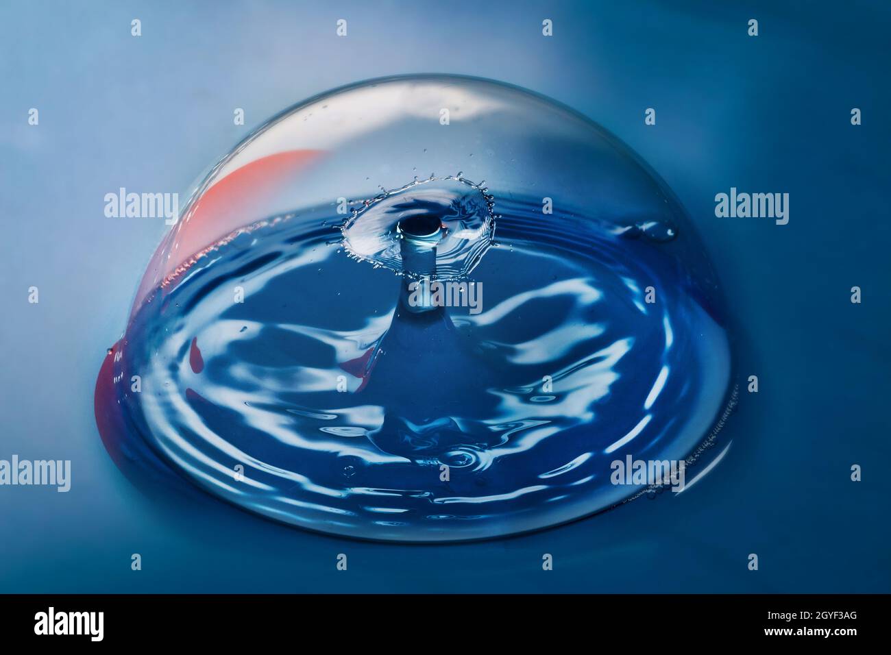 Superficie blu con bolla pulita contenente increspature da due gocce d'acqua che si scontrano nell'aria Foto Stock