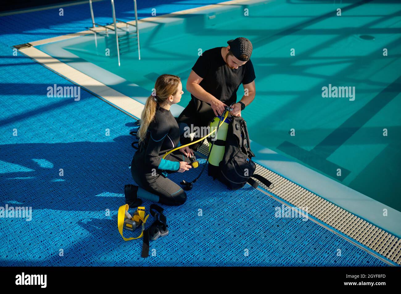 L'istruttore maschile in tuta spiega come funziona l'attrezzatura subacquea, scuola di immersioni. Insegnare alle persone a nuotare sott'acqua, piscina interna Foto Stock