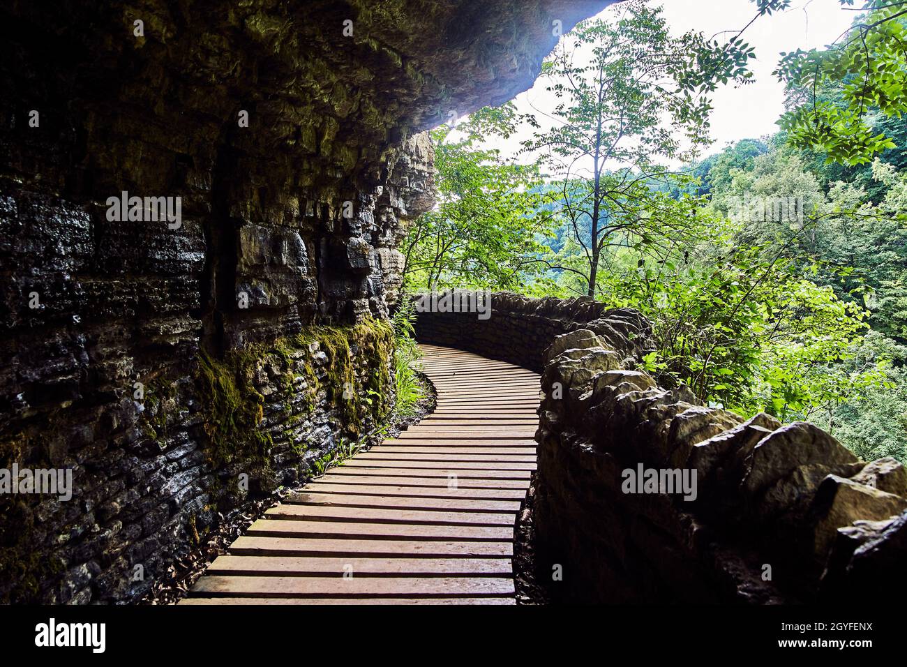 Passerella in legno con muro di pietra che si avvolge intorno alle pareti della scogliera Foto Stock