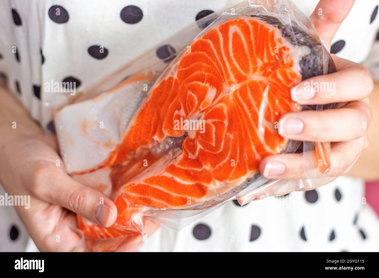 Pesce salmone rosso crudo fetta nel pacchetto in donna caucasica mani su sfondo chiaro primo piano. Foto Stock