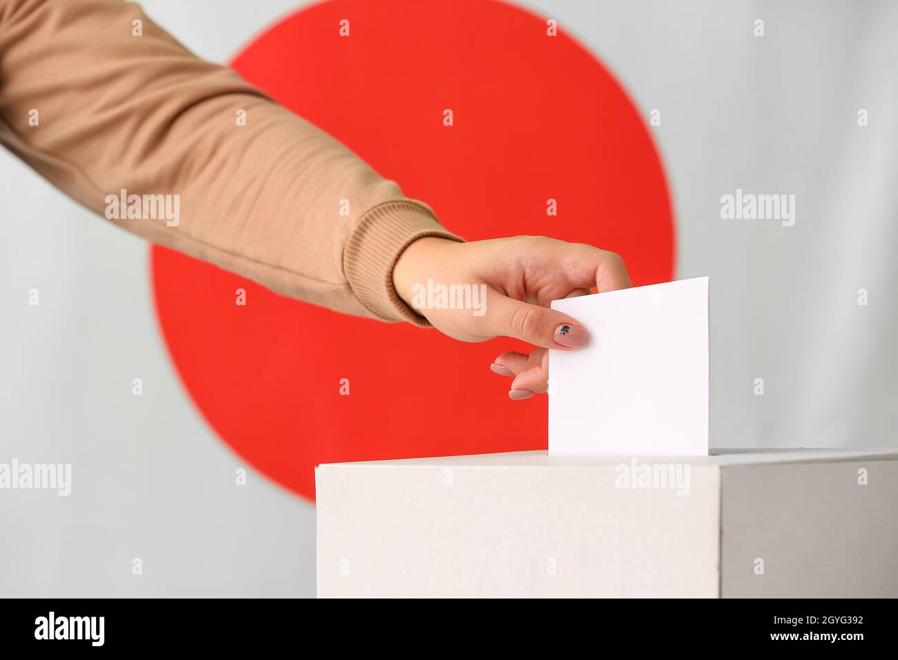 Donna che vota vicino alle urne contro la bandiera del Giappone Foto Stock