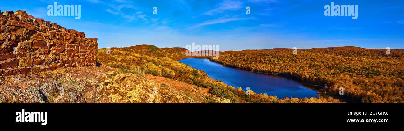 Panorama del lago gigante circondato da un'infinita collina di una foresta in autunno e un muro di mattoni sulla sinistra Foto Stock