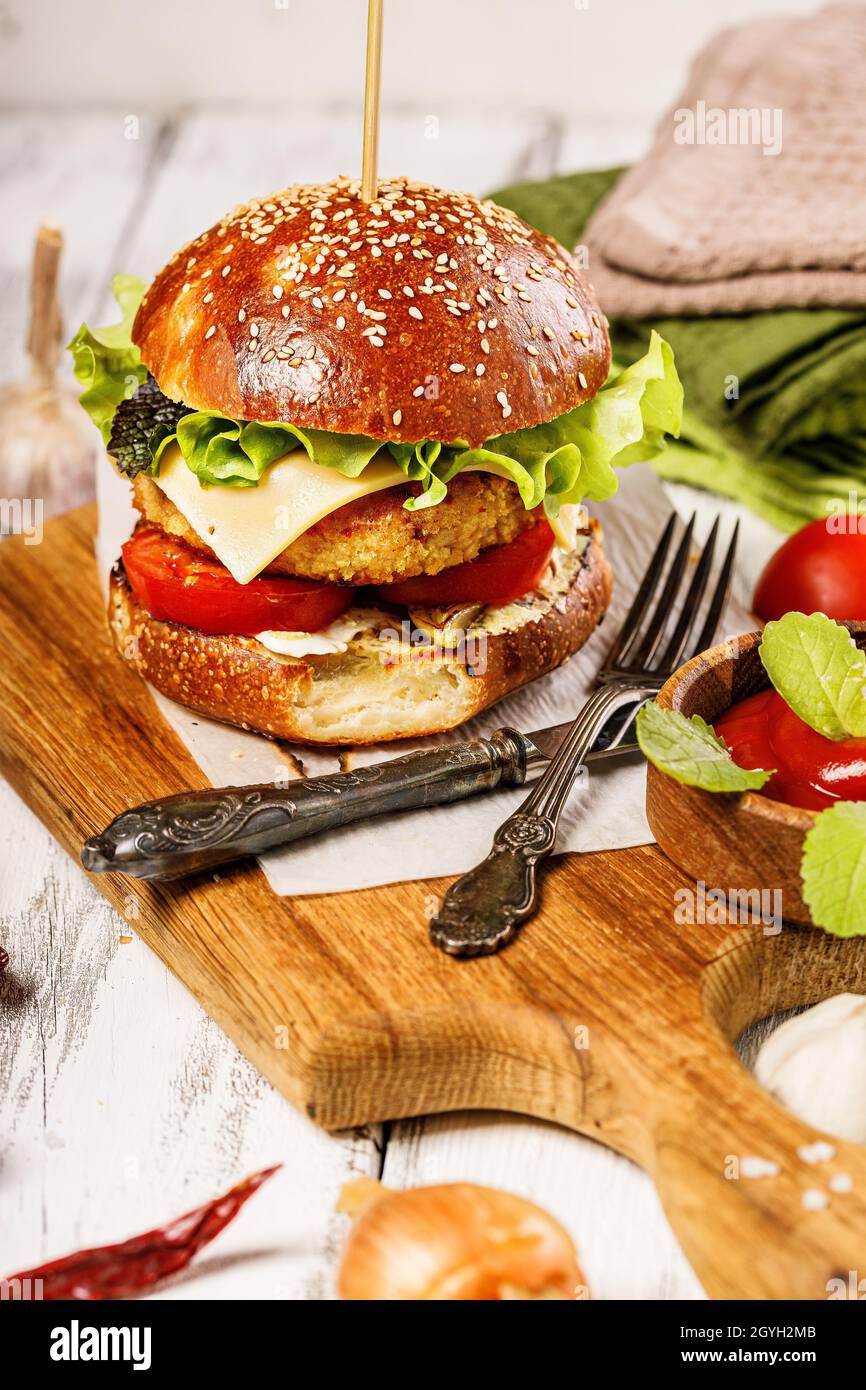 Appetitoso hamburger di pollo con formaggio, insalata fresca e verdure su un tagliere. Foglie di lattuga fresca, pomodori e cipolle. Tradizionale americano Foto Stock