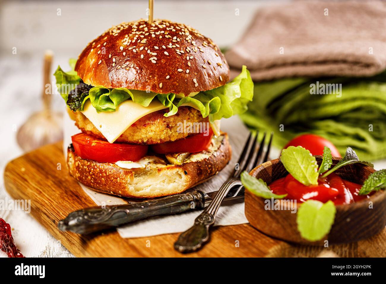 Hamburger di pollo appetitoso fatto in casa con formaggio, insalata fresca e verdure su un tagliere. Foglie di lattuga fresca, pomodori e cipolle. Tradizionale Foto Stock