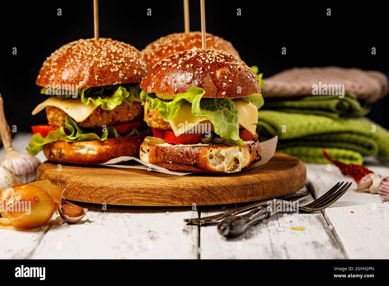 Hamburger di pollo appetitoso fatto in casa con formaggio, insalata fresca e verdure su un tagliere rotondo. Foglie di lattuga, pomodori e cipolle. Tradizionale Foto Stock