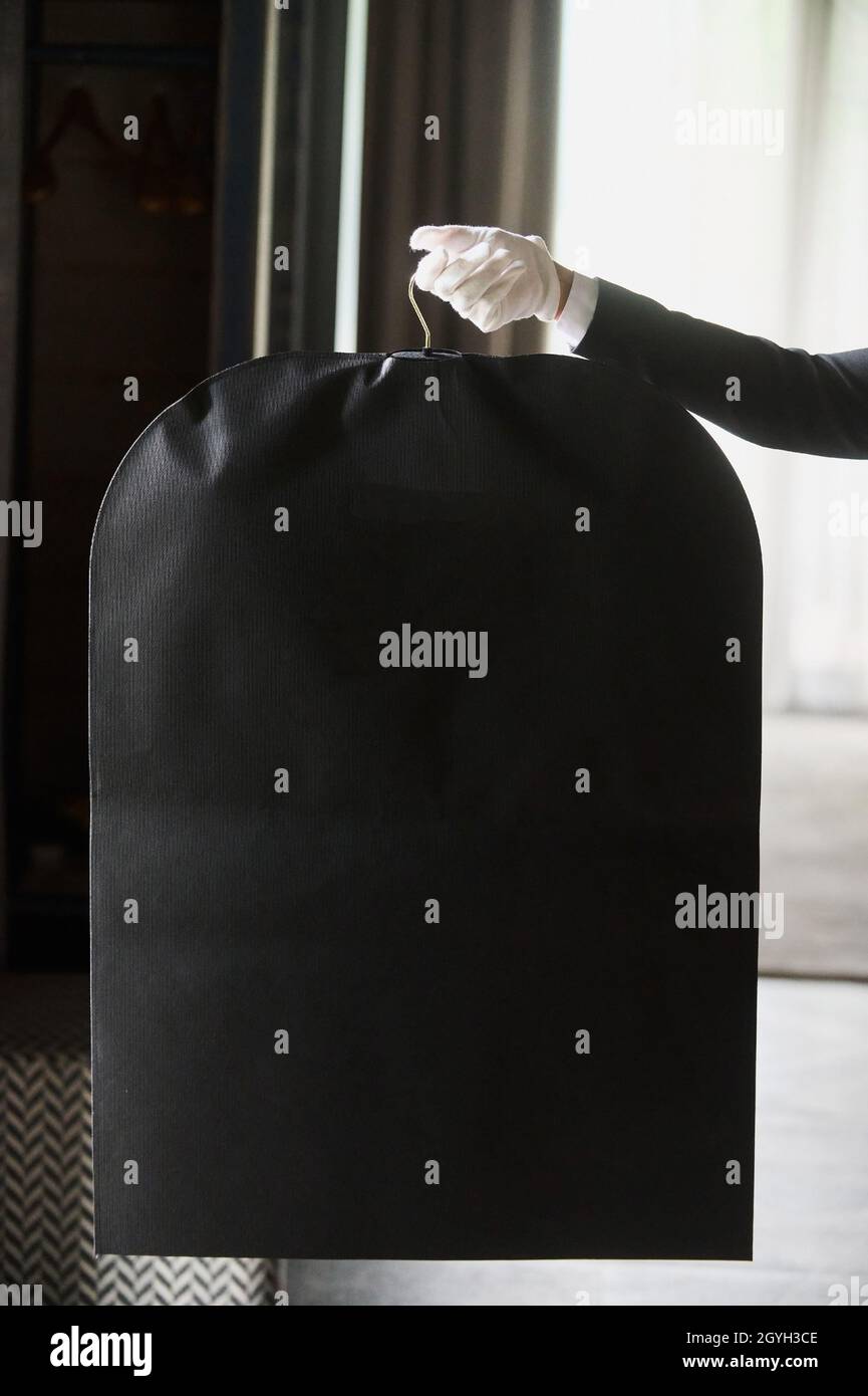 Vestito nero, borsa da viaggio. Le mani di un lavoratore alberghiero in guanti bianchi Foto Stock
