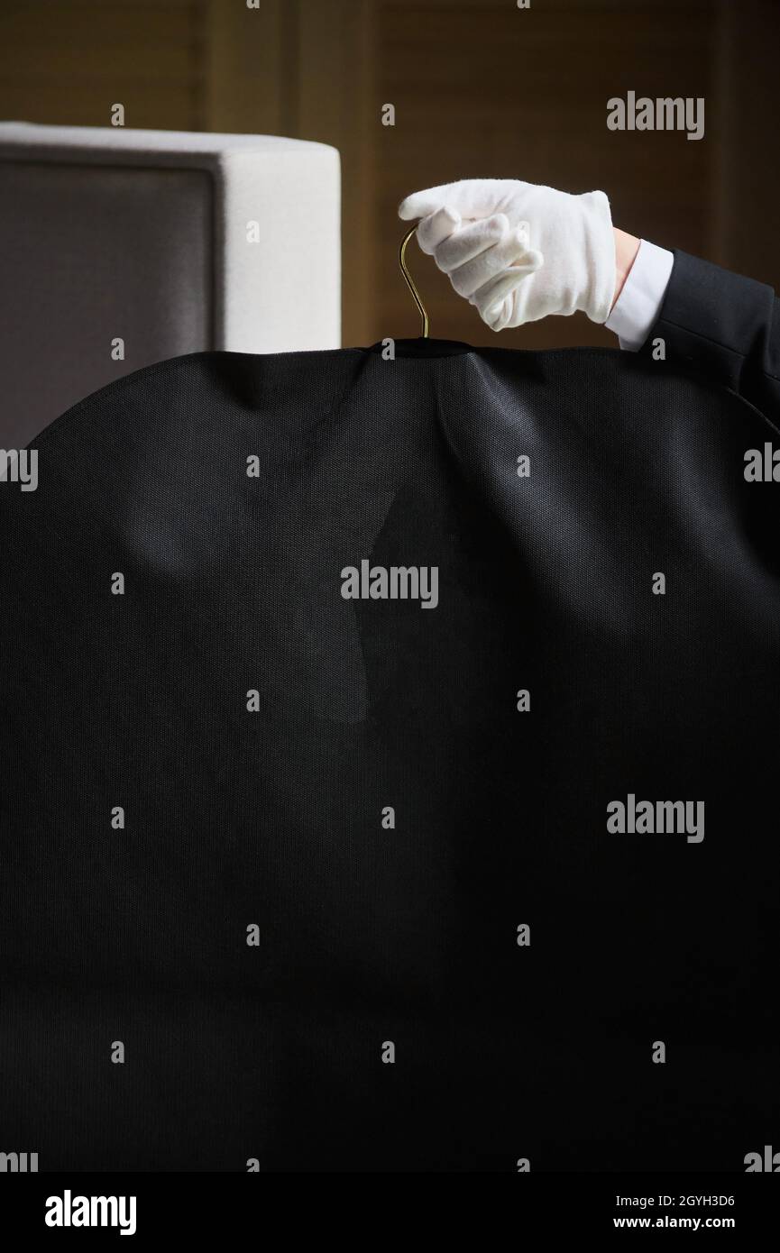 Vestito nero, borsa da viaggio. Le mani di un lavoratore alberghiero in guanti bianchi Foto Stock