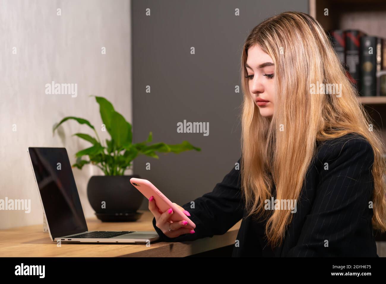 Donna d'affari che controlla i messaggi o guarda i contenuti multimediali sul suo smartphone mentre lavora alla sua scrivania in ufficio Foto Stock