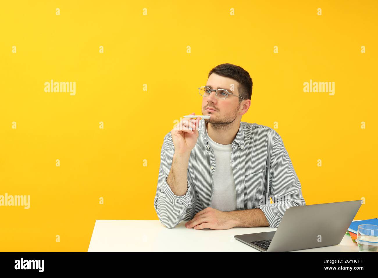 Studiare il concetto con il giovane seduto sul tavolo su sfondo giallo. Foto Stock
