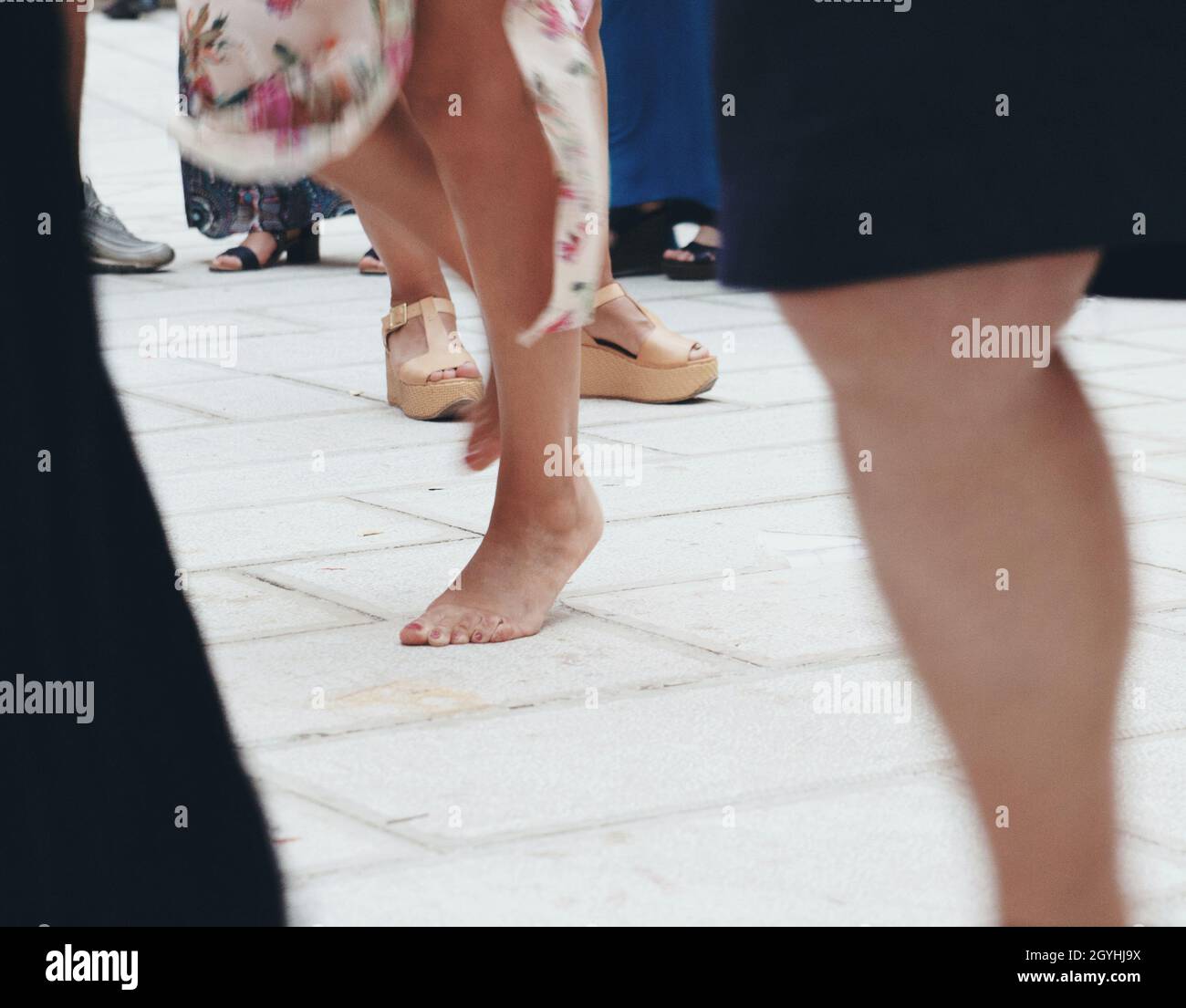 Giovane donna che balla a piedi nudi sulla strada della città tra una folla di persone, celebrare la vita, godersi un momento felice, divertirsi all'aria aperta, vista ravvicinata. Weddin Foto Stock