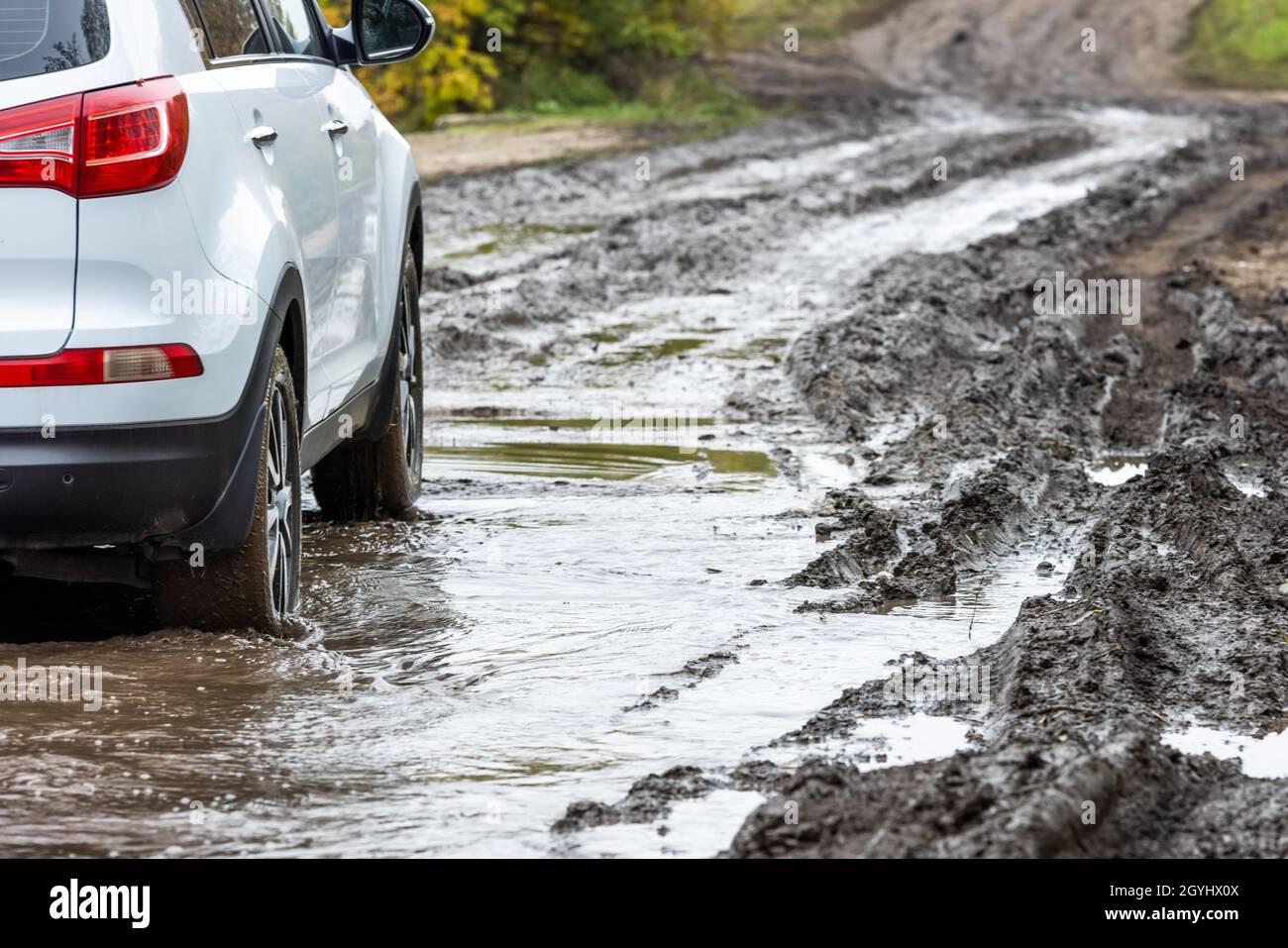 pulire l'auto suv bianca che si muove su strada sterrata con argilla bagnata davanti a una pendenza sfocata Foto Stock