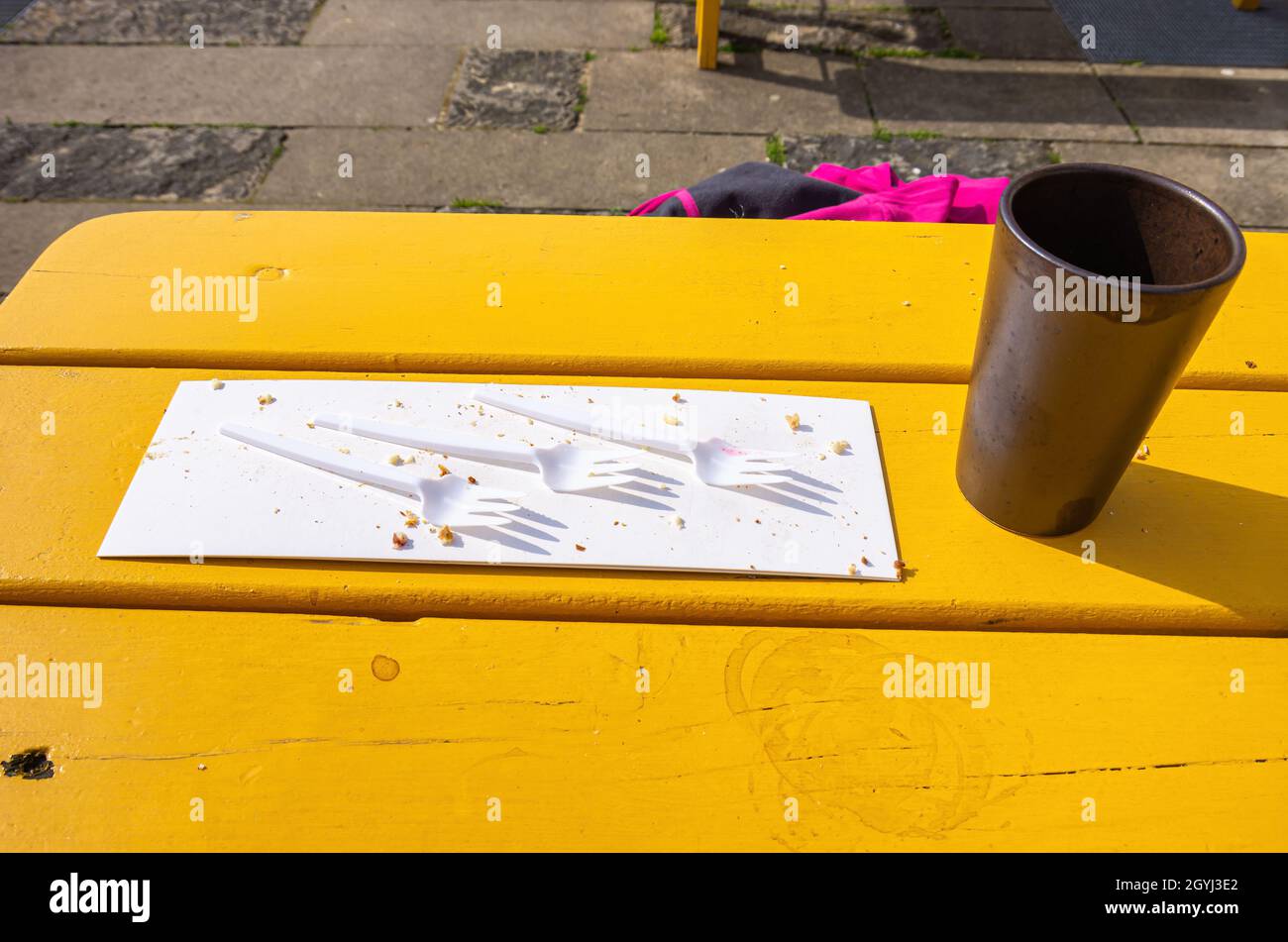Tre forchette di plastica su un pezzo di cartone con briciole per torte e una tazza di caffè vuota su un tavolo di legno giallo. Foto Stock