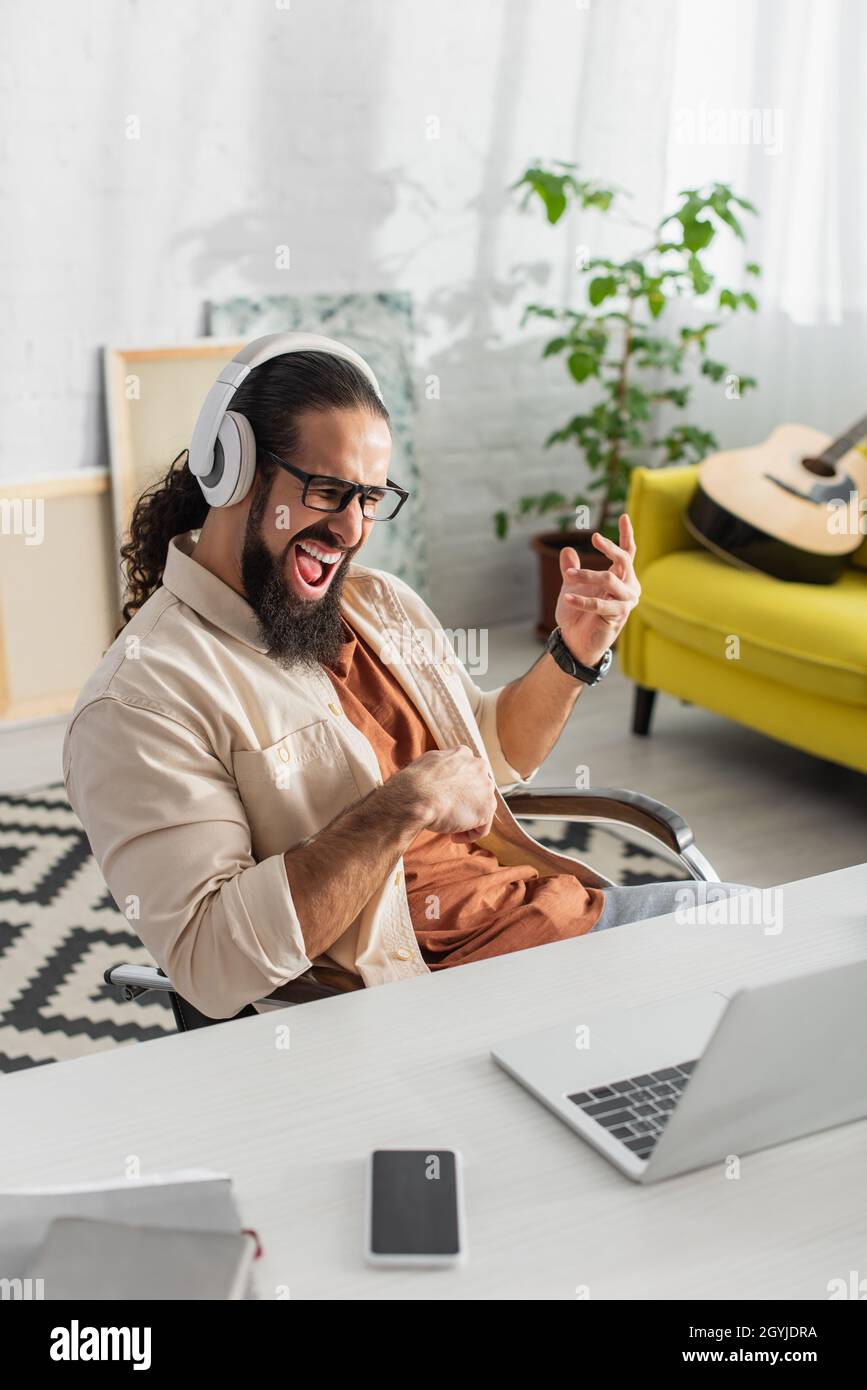 entusiasta freelance ispanico in cuffie urla mentre ascolti musica vicino al laptop Foto Stock