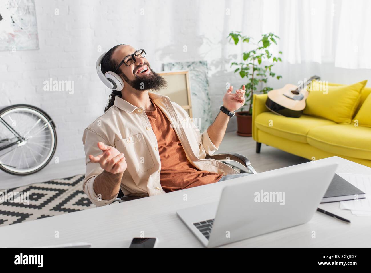 contento latino freelance in cuffie ascoltare musica vicino al portatile a casa Foto Stock