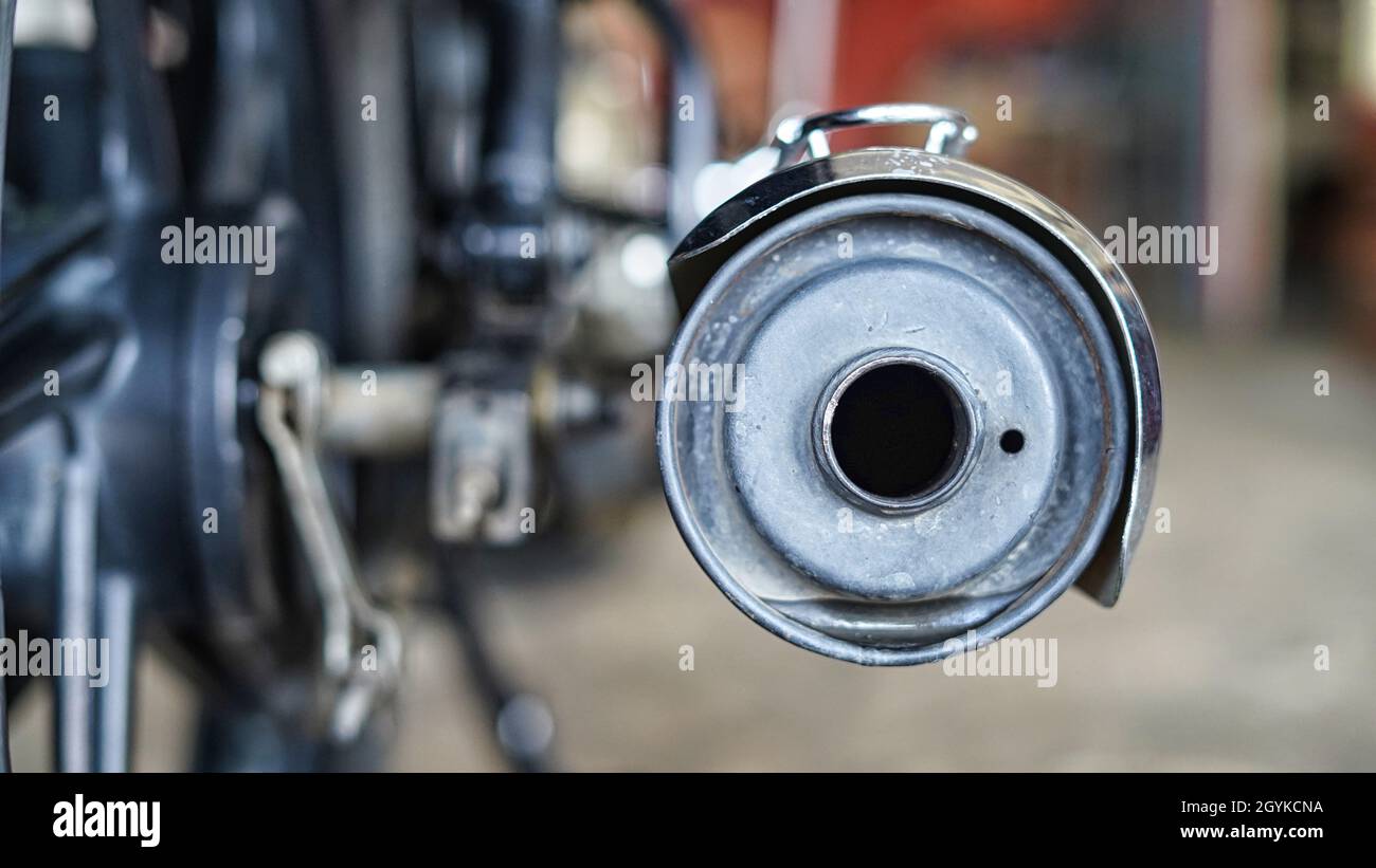 Focalizzazione selettiva su un tappo terminale del silenziatore per motociclette con sfondo sfocato dell'officina. Foto Stock