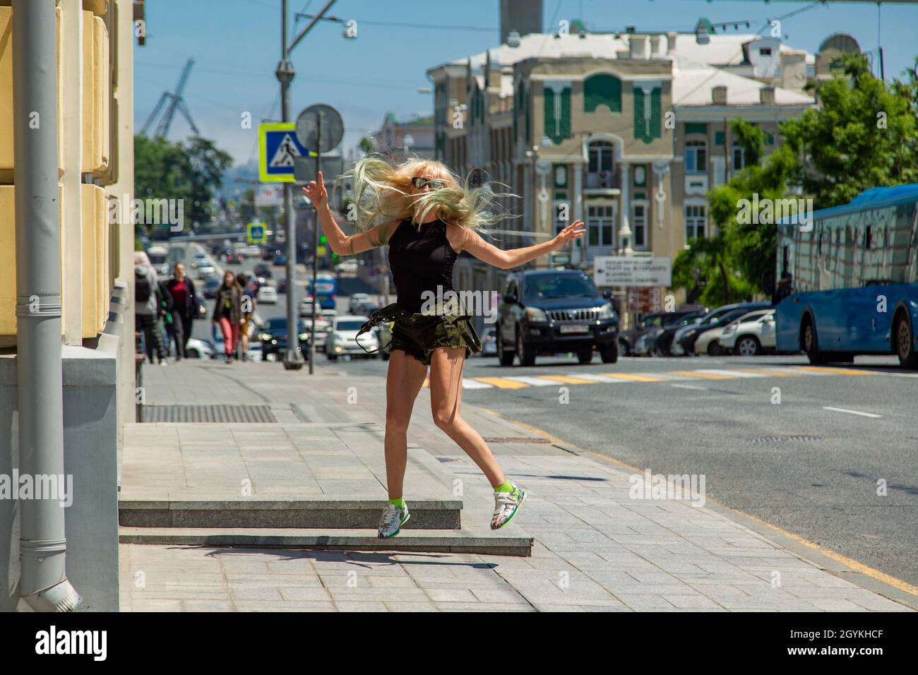 Una giovane ragazza in occhiali e shorts kaki rimbalza sulla strada lungo la strada. Una buona bionda. Foto Stock
