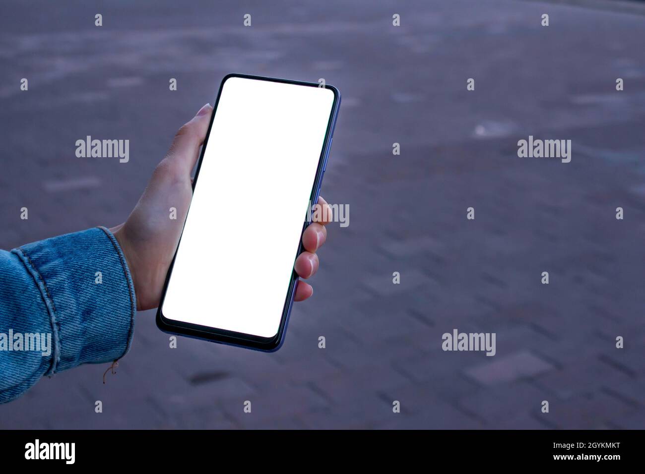 Donna con smartphone nero. Immagine mockup di una mano donna che tiene il telefono cellulare con schermo bianco bianco vuoto del desktop mentre si cammina sul marciapiede. Foto Stock
