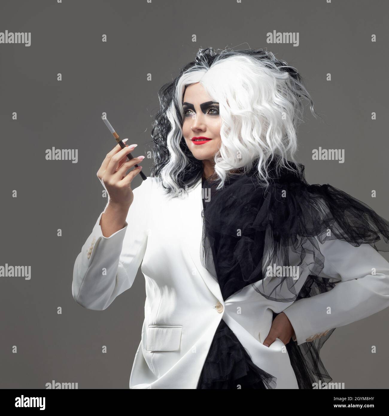 Una donna carismatica insolita in un abito bianco e nero con capelli bianchi e neri fuma una sigaretta utilizzando un boccaglio, un'immagine audace ed elegante di un Foto Stock