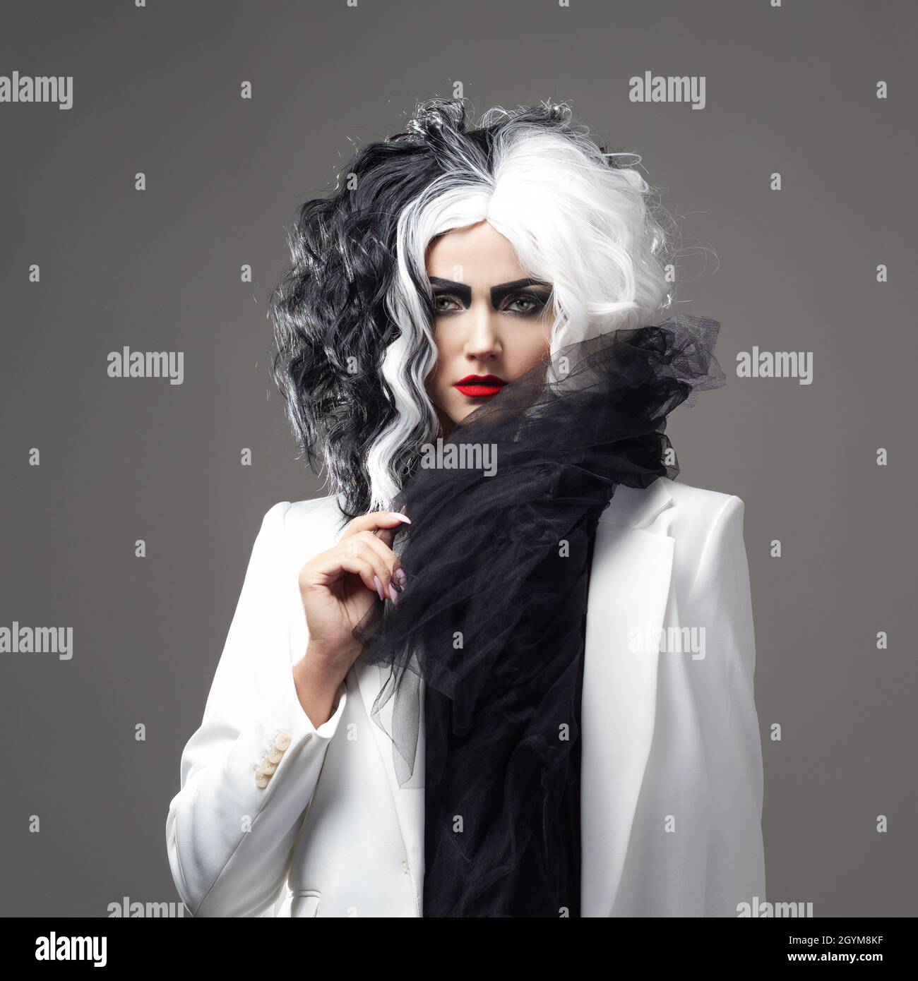 Una donna carismatica insolita in un abito bianco e nero con capelli bianchi e neri, un'immagine audace ed elegante di un criminale per Halloween Foto Stock