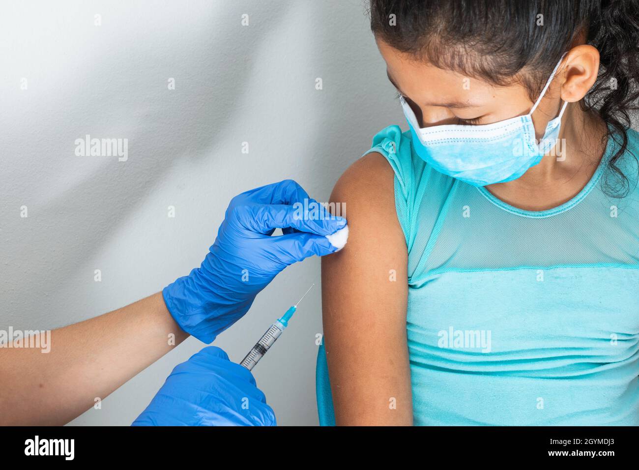 l'infermiera dei bambini pulendo il sangue con la lana di cotone dopo la somministrazione dell'iniezione nel braccio della ragazza marrone. il medico iniettando il vaccino contro covid-19. influenza vacci Foto Stock