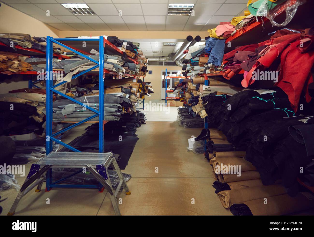 Deposito con file di ripiani pieni di rotoli di tessuto e pelle presso la fabbrica di calzature Foto Stock