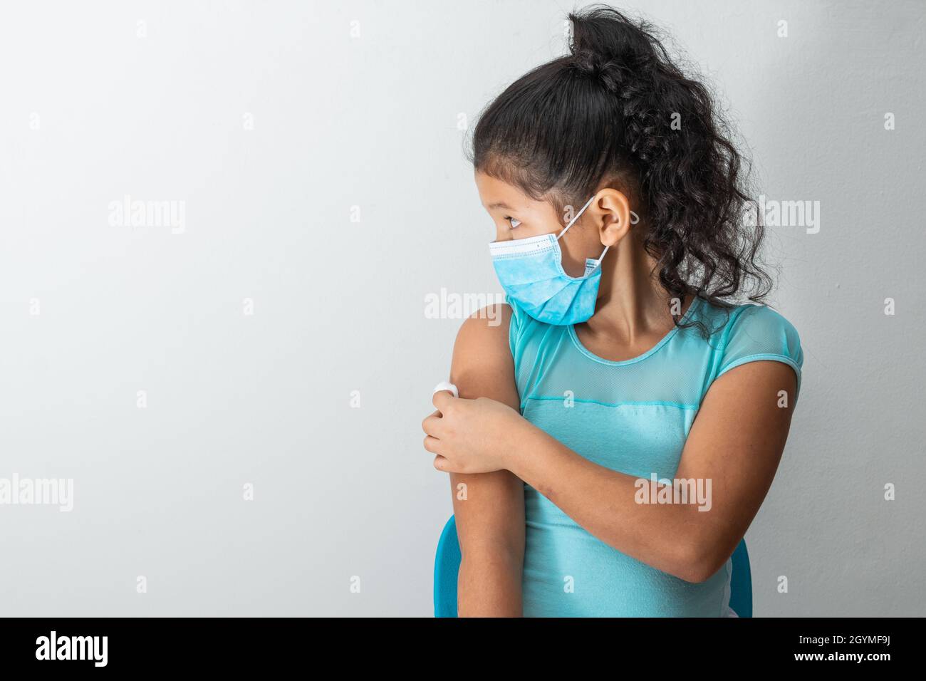 bambina che guarda a destra come lei tiene una palla di cotone sul suo braccio dopo aver ferito la pelle o iniettato il vaccino covid-19. Pronto soccorso. Medico, phar Foto Stock