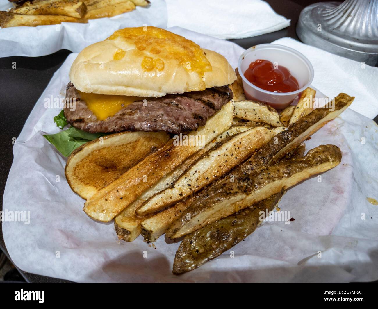 Vista inclinata verso il basso di un grassoso cheeseburger e patatine fritte croccanti, servite in un cestino in un'immersione con hamburger locale Foto Stock