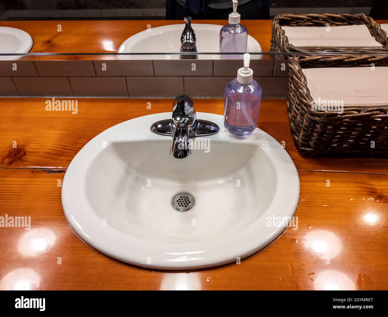 Vista ad angolo di un lavandino bianco su un bancone in legno all'interno di un bagno del ristorante Foto Stock