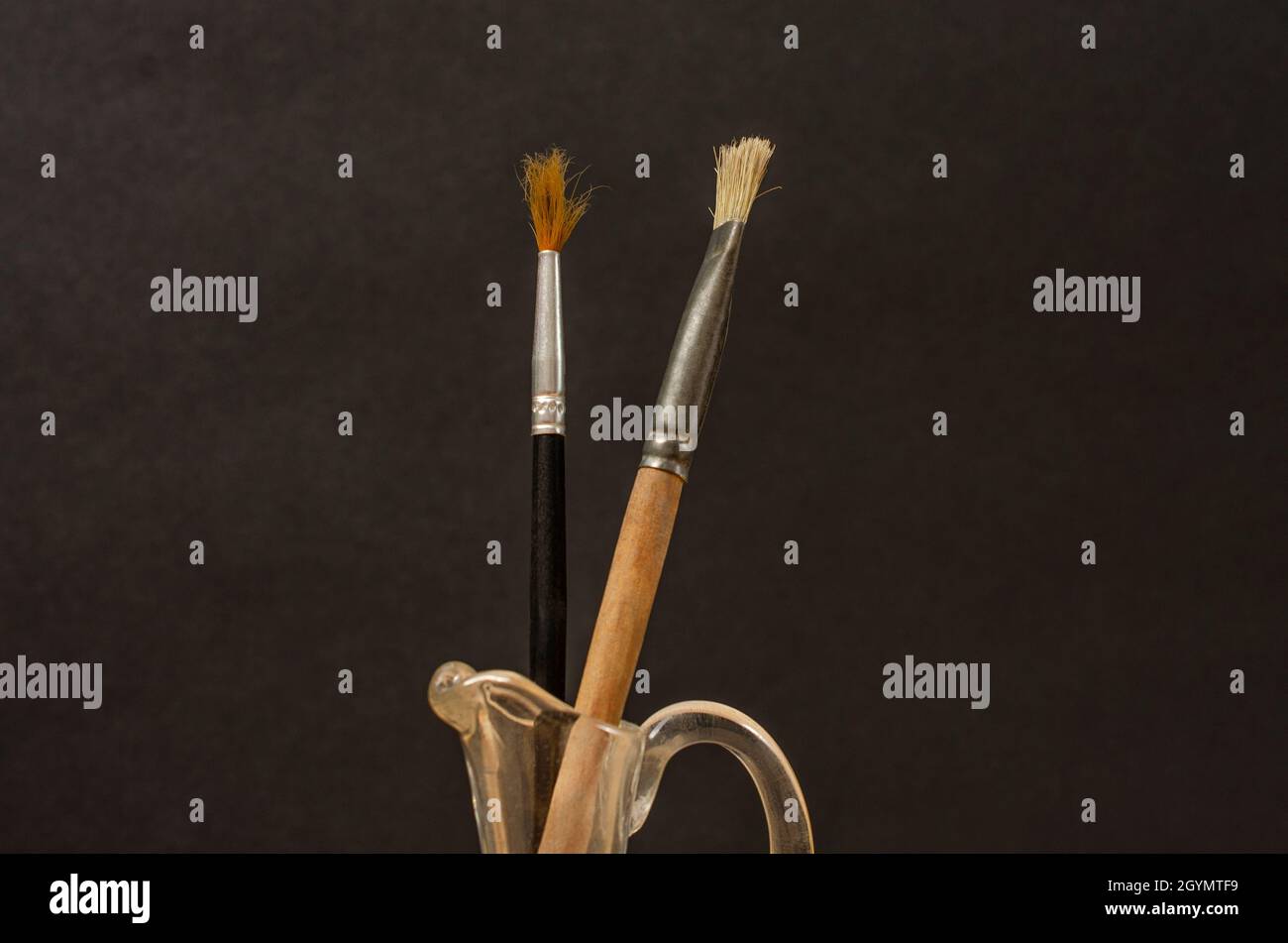 Vecchie spazzole per pittura artistica usate in vaso di vetro terto. Vita morta. Composizione minimalista con sfondo nero. Foto Stock