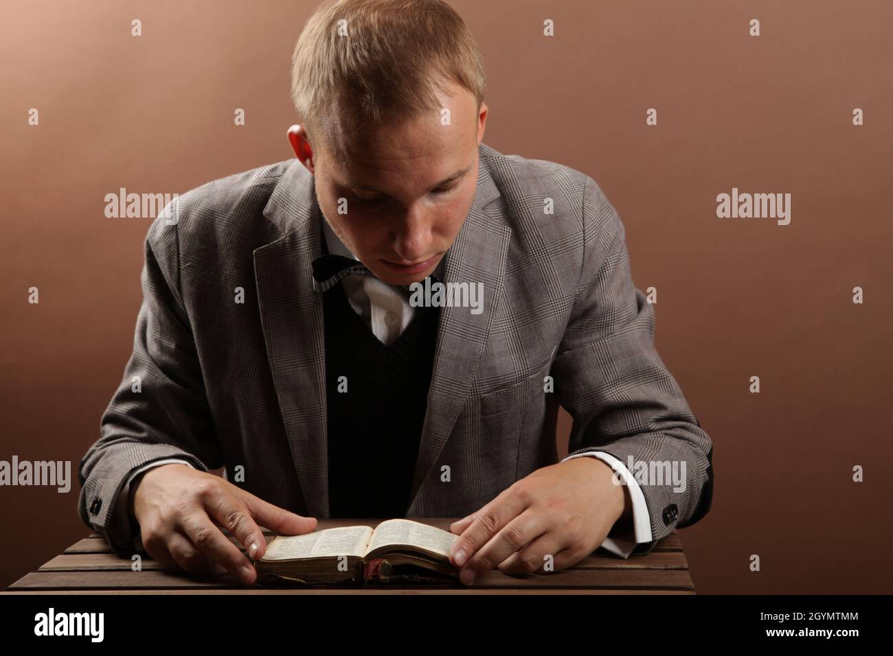 Un uomo d'affari bello e sicuro in un vestito, seduto da solo su uno sfondo marrone e leggendo un libro. Accanto ad un tavolo di legno. Foto di alta qualità Foto Stock