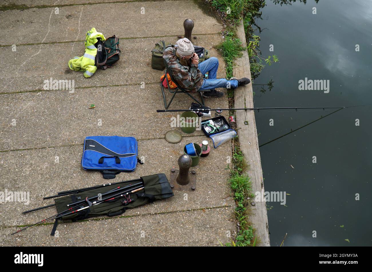 Uomo più anziano che pesca con affrontare intorno a lui l'illuminazione di una sigaretta. Foto Stock