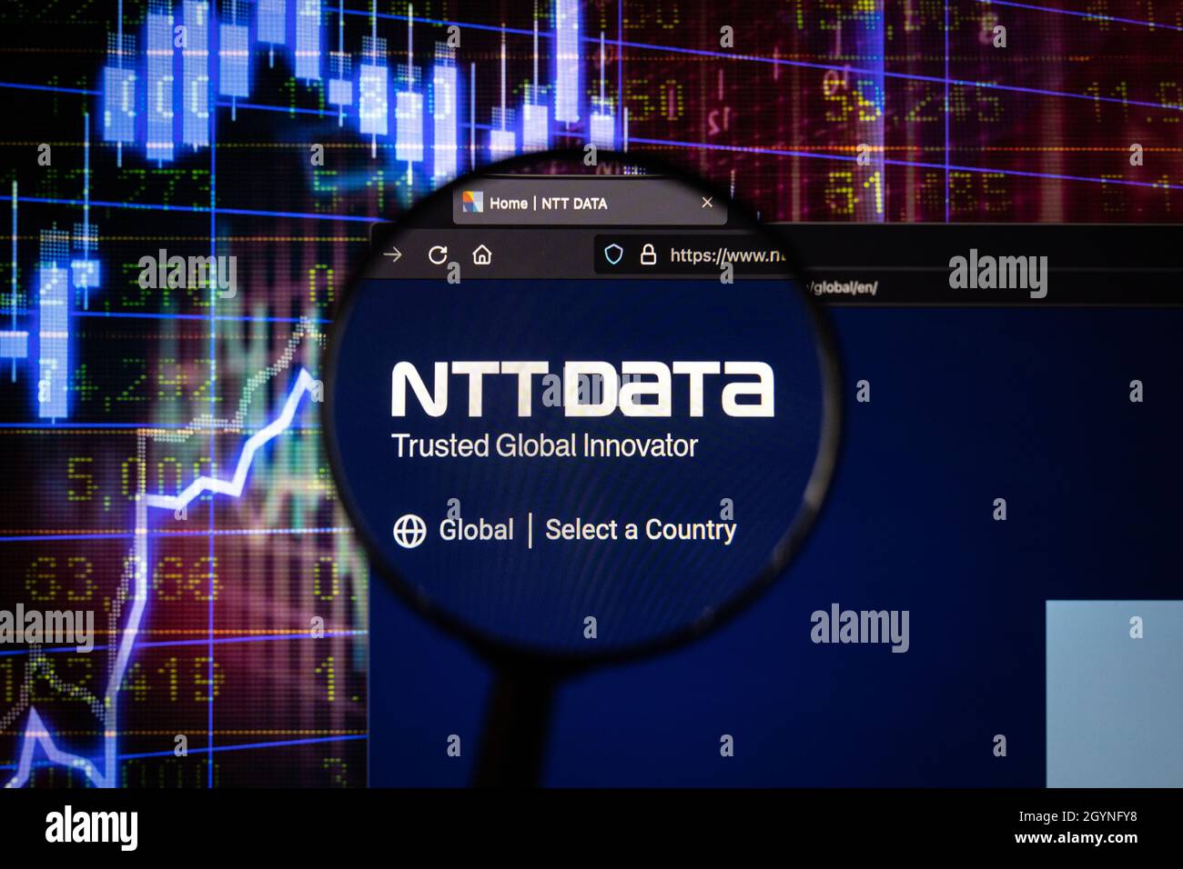 NTT Data Company logo su un sito web con blurry mercato azionario sviluppi in background, visto su uno schermo del computer attraverso una lente d'ingrandimento Foto Stock