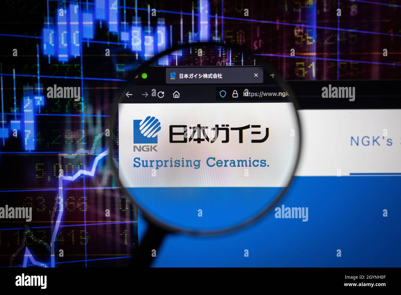 Logo NGK azienda su un sito web con blurry sviluppi del mercato azionario in background, visto su uno schermo del computer attraverso una lente d'ingrandimento Foto Stock