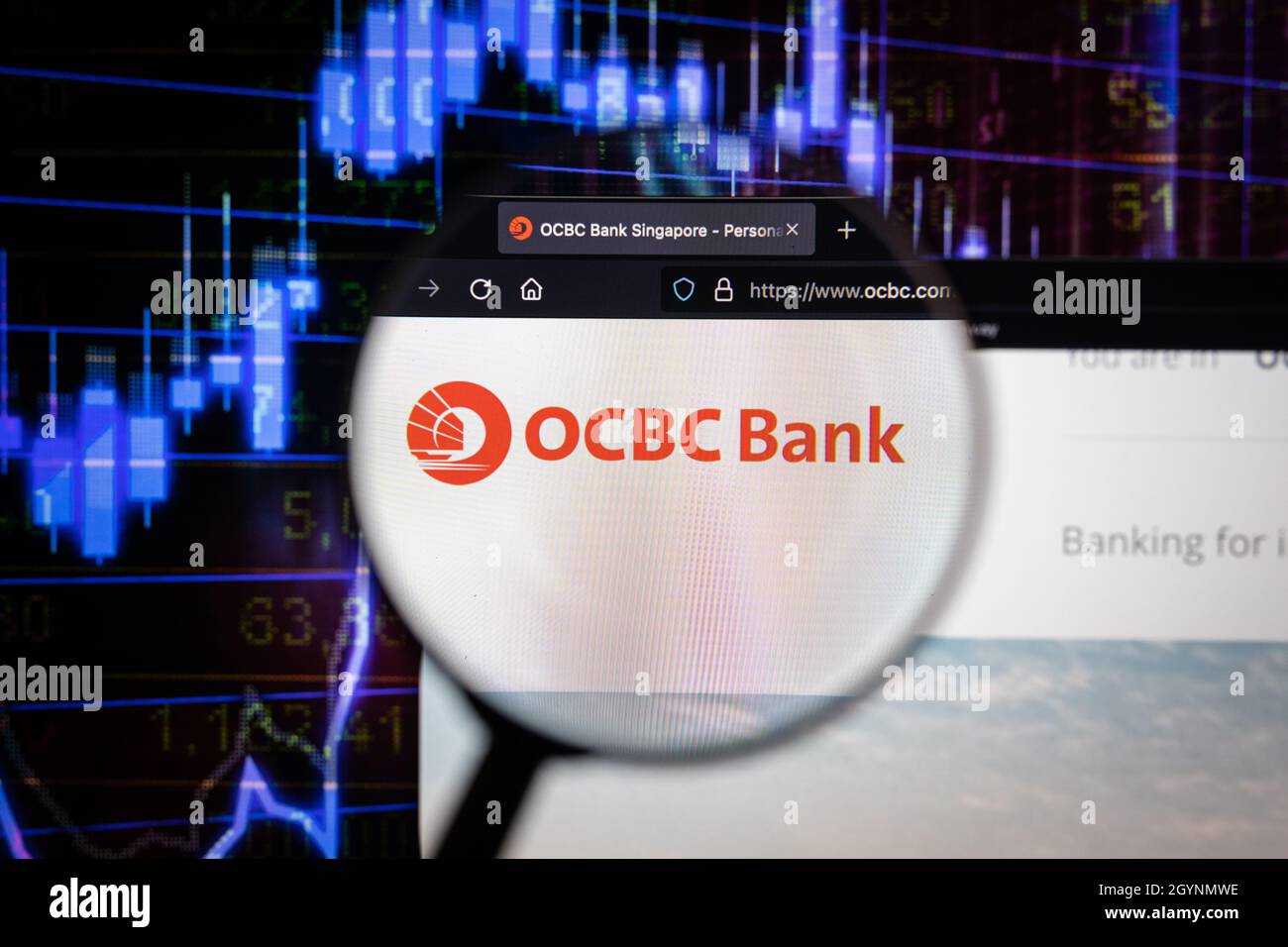 OCBC Bank Company logo su un sito web con blurry mercato azionario sviluppi in background, visto su uno schermo di computer attraverso una lente d'ingrandimento Foto Stock
