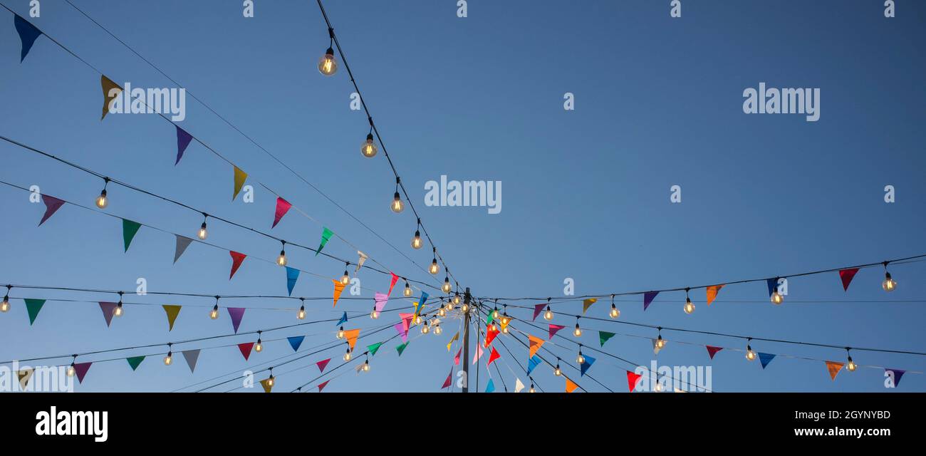 Garland con pennanti colorati e lampadine su palo sopra il cielo blu. Formato lungo Foto Stock