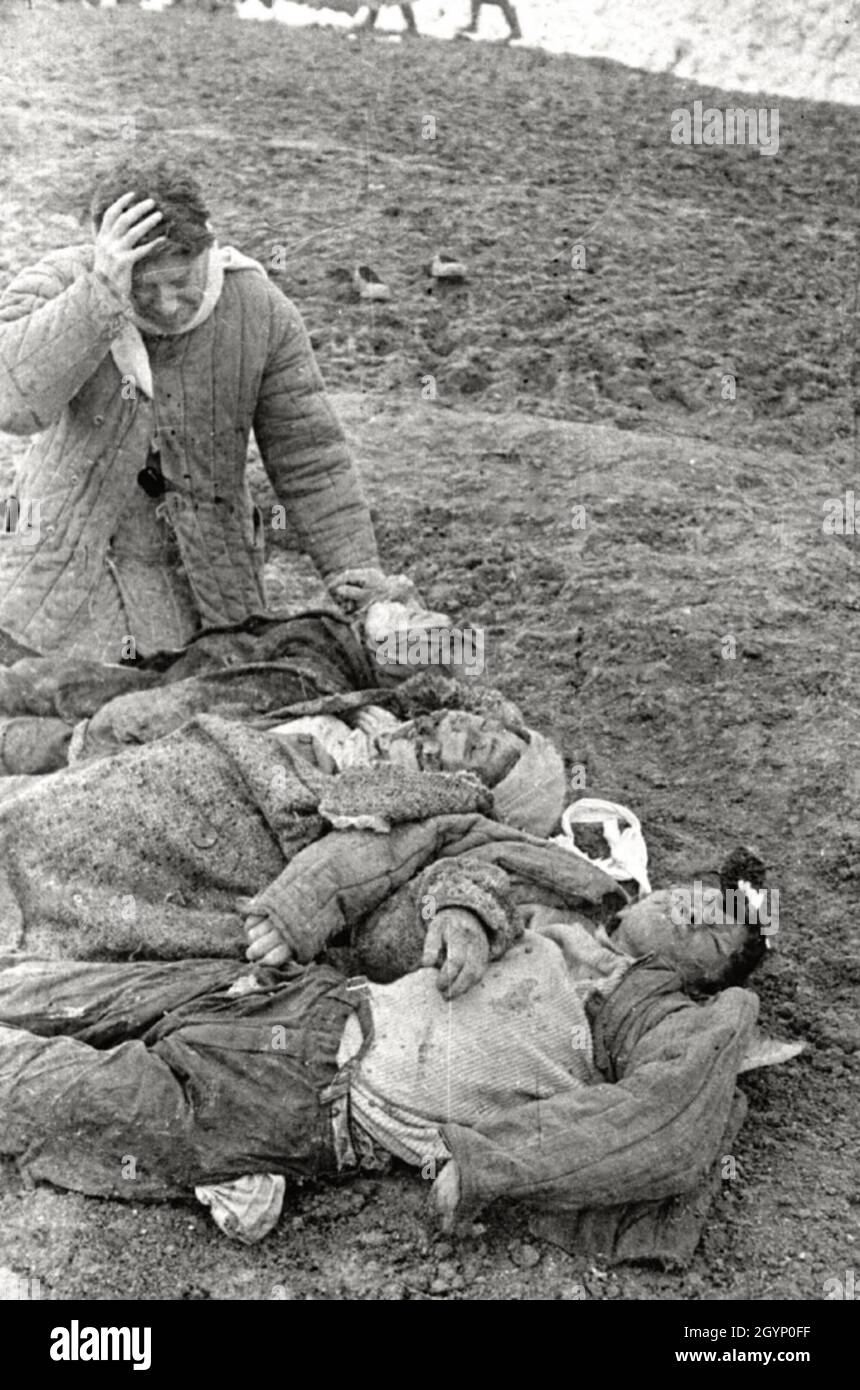 Un'immagine angosciante di un uomo che tiene il capo incredulamente mentre guarda i corpi della sua famiglia, assassinati dai nazisti nell'URSS. Foto Stock