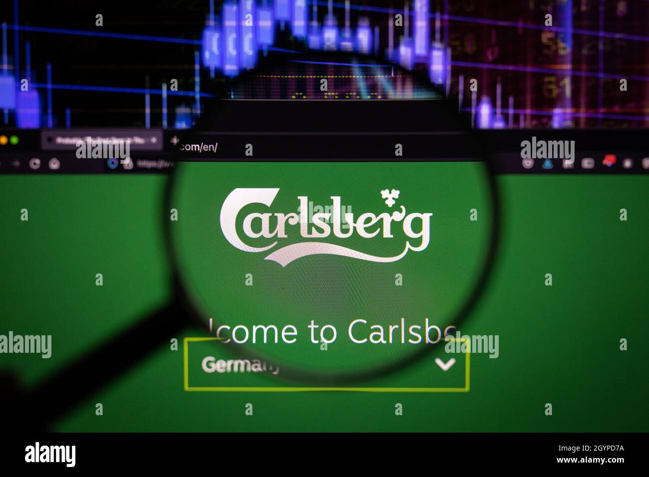 Il logo della società Carlsberg su un sito web con sviluppi del mercato azionario sfocati in background, visto su uno schermo del computer attraverso una lente d'ingrandimento Foto Stock
