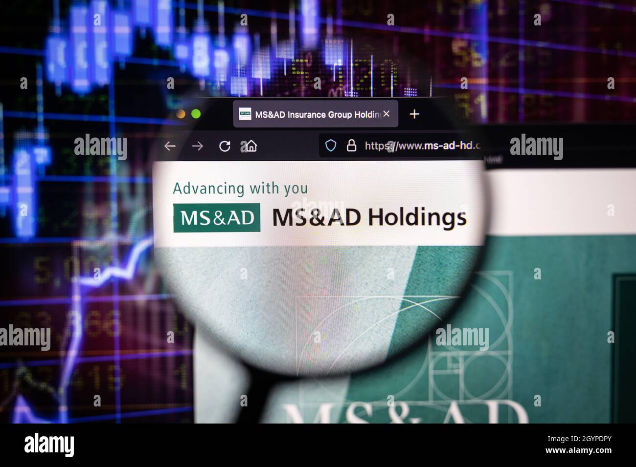 MS&ad Holdings Company logo su un sito web con blurry stock market grafici sullo sfondo, visto su uno schermo del computer attraverso una lente d'ingrandimento. Foto Stock