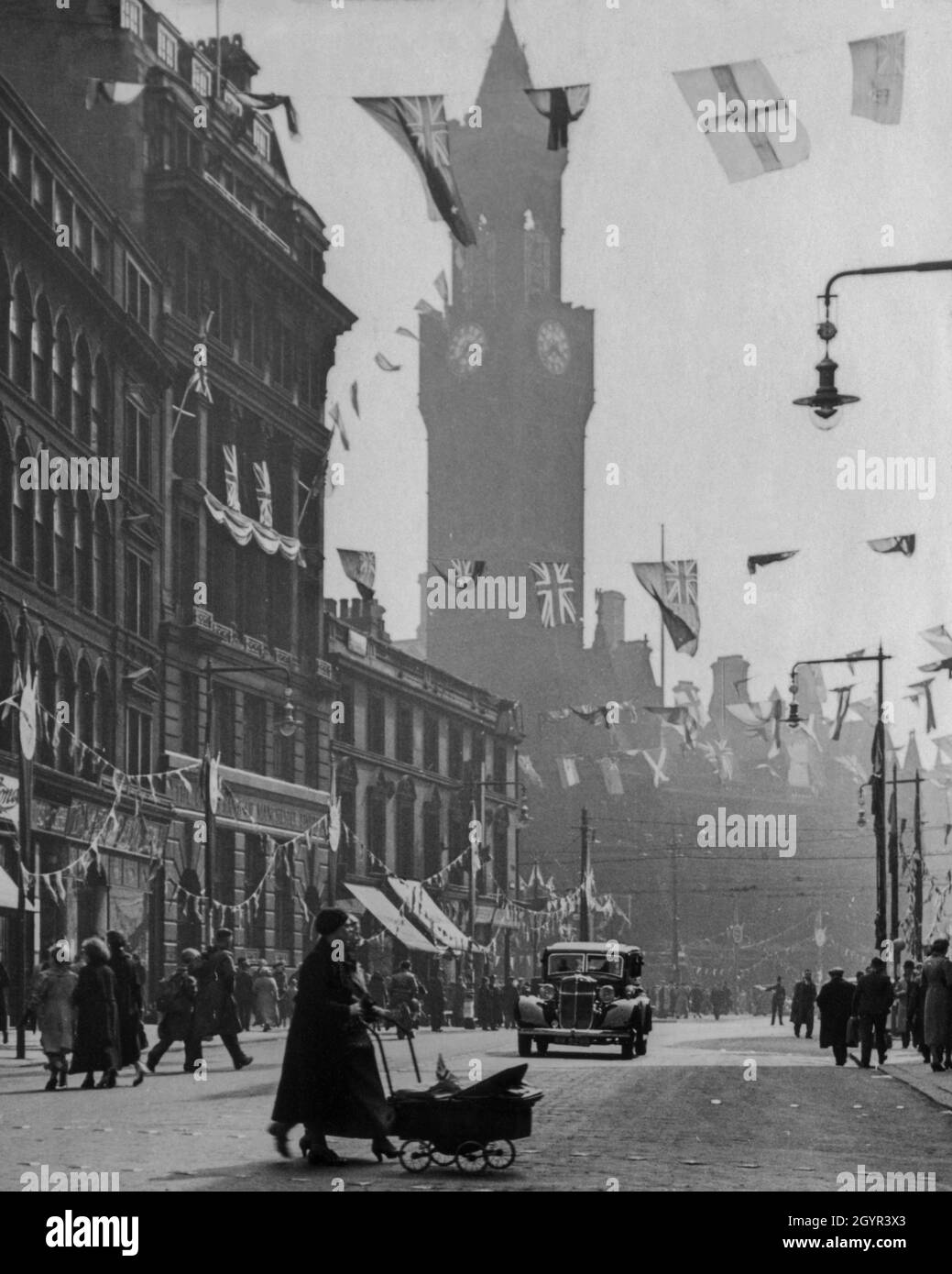 Una strada nel centro di Bradford, Yorkshire, in Inghilterra, addobbata di bandiere e bunting per celebrare l'incoronazione del monarca britannico, re Giorgio vi, il 12 maggio 1937. La torre dell'orologio di 200 piedi in stile toscano o campanile del Municipio di Bradford del XIX secolo (precedentemente Bradford Town Hall) sorge sullo sfondo. Fotografia d'epoca da una collezione privata. Foto Stock