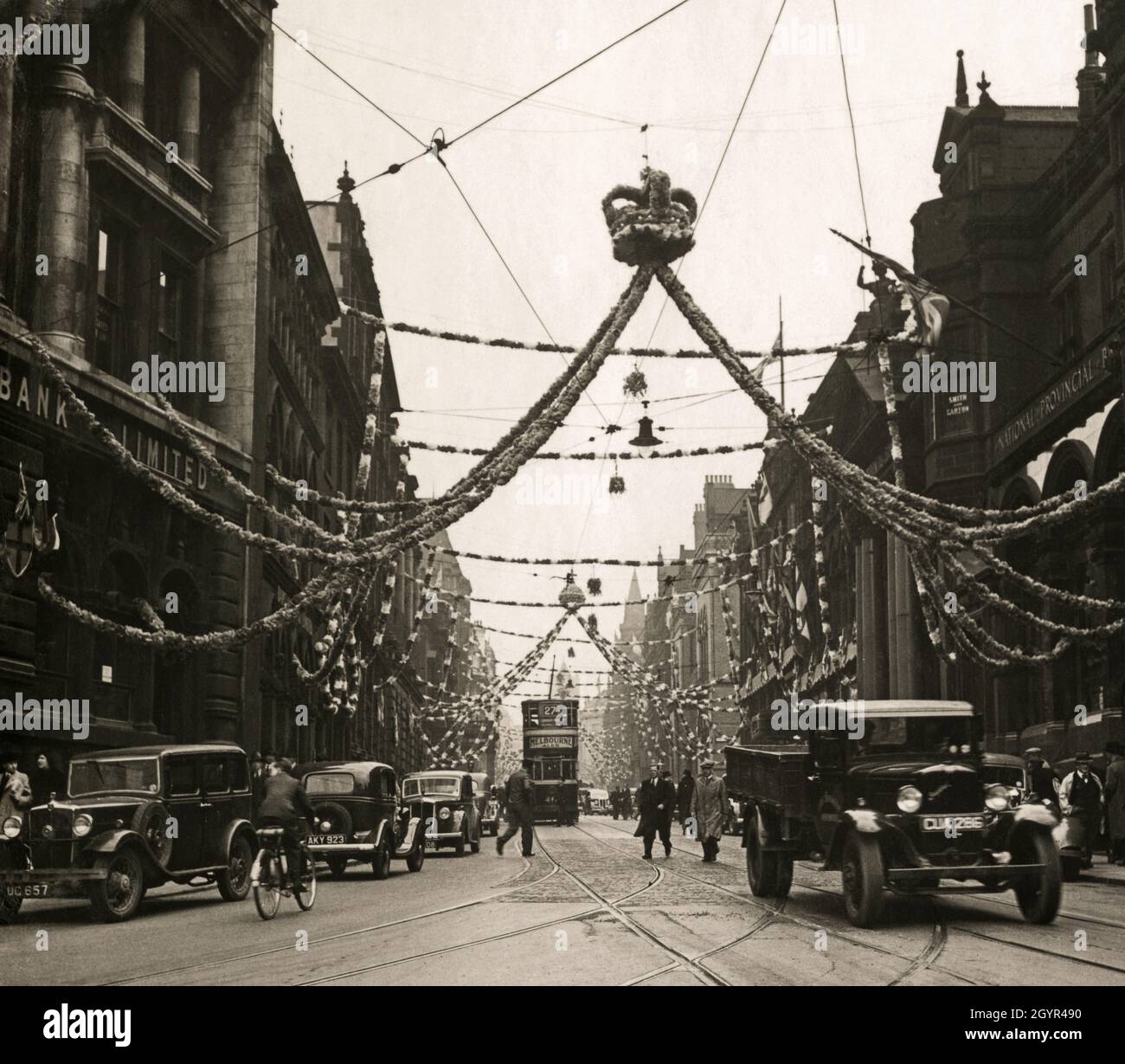 Un filobus a due piani e una gamma di veicoli a motore degli anni '30 nel centro di Leeds, Yorkshire, Inghilterra, sotto le decorazioni per celebrare l'incoronazione del monarca britannico, King George VI, il 12 maggio 1937 Foto Stock