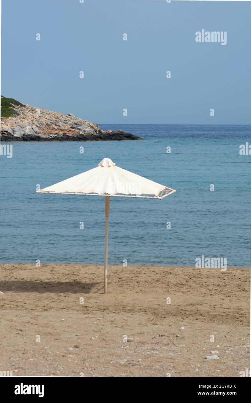 Ombrellone in spiaggia presso l'isola greca appartata di Sikinos Sand, mare e cielo blu foto verticale con spazio copia Foto Stock
