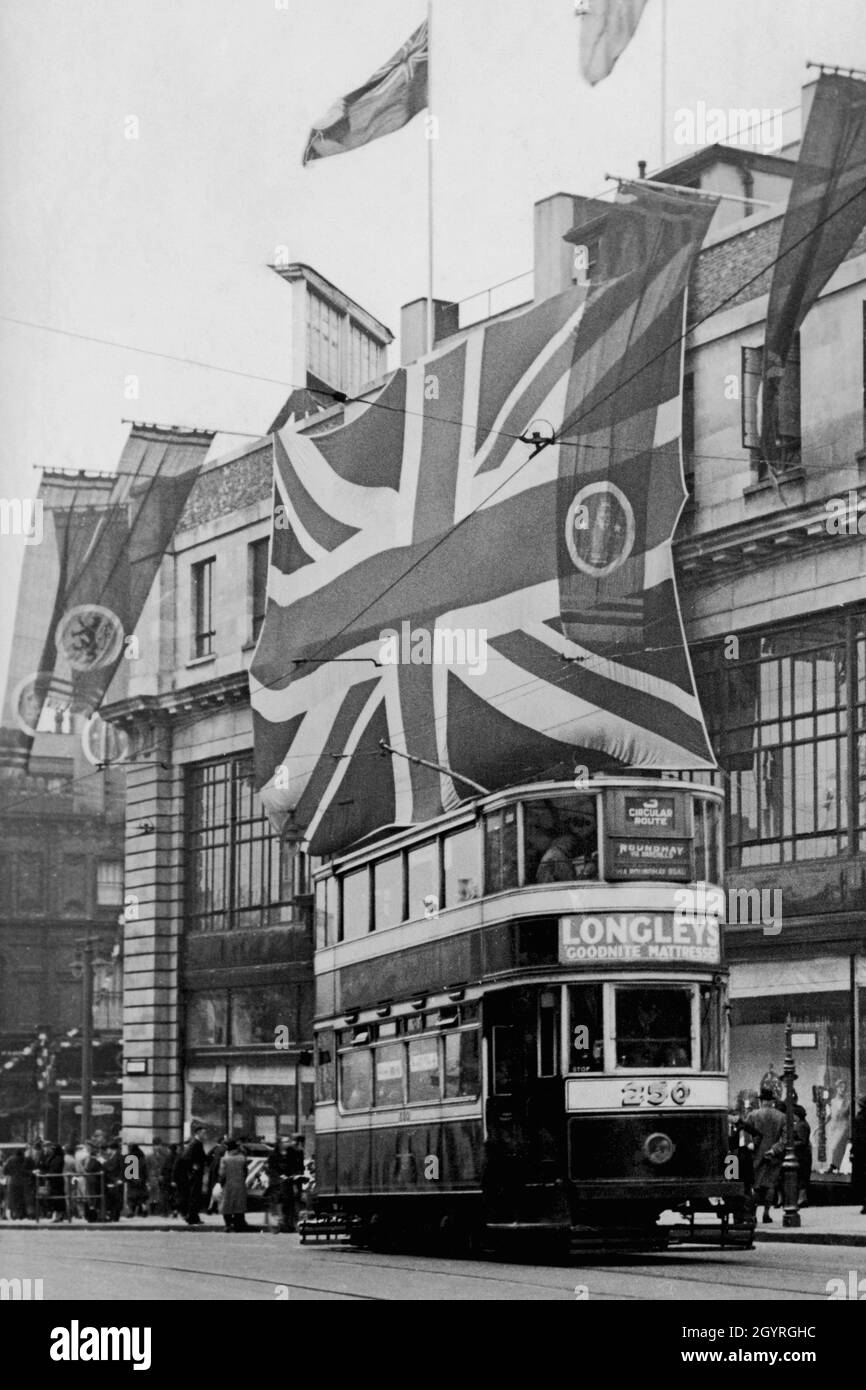 Pubblicità per materassi di fronte al filobus a due piani su un percorso circolare nel centro di Leeds, sotto l'enorme Union Jack che celebra l'incoronazione del monarca britannico, re Giorgio vi, il 12 maggio 1937. Fotografia d'epoca da una collezione privata. Foto Stock