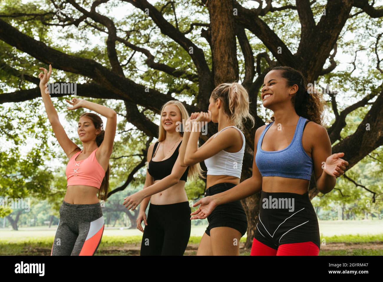 felice giovane multietnica donne adolescenti amici gruppo rilassarsi e ballare dopo l'esercizio nel parco al fine settimana mattina. vita dopo covid. Foto Stock