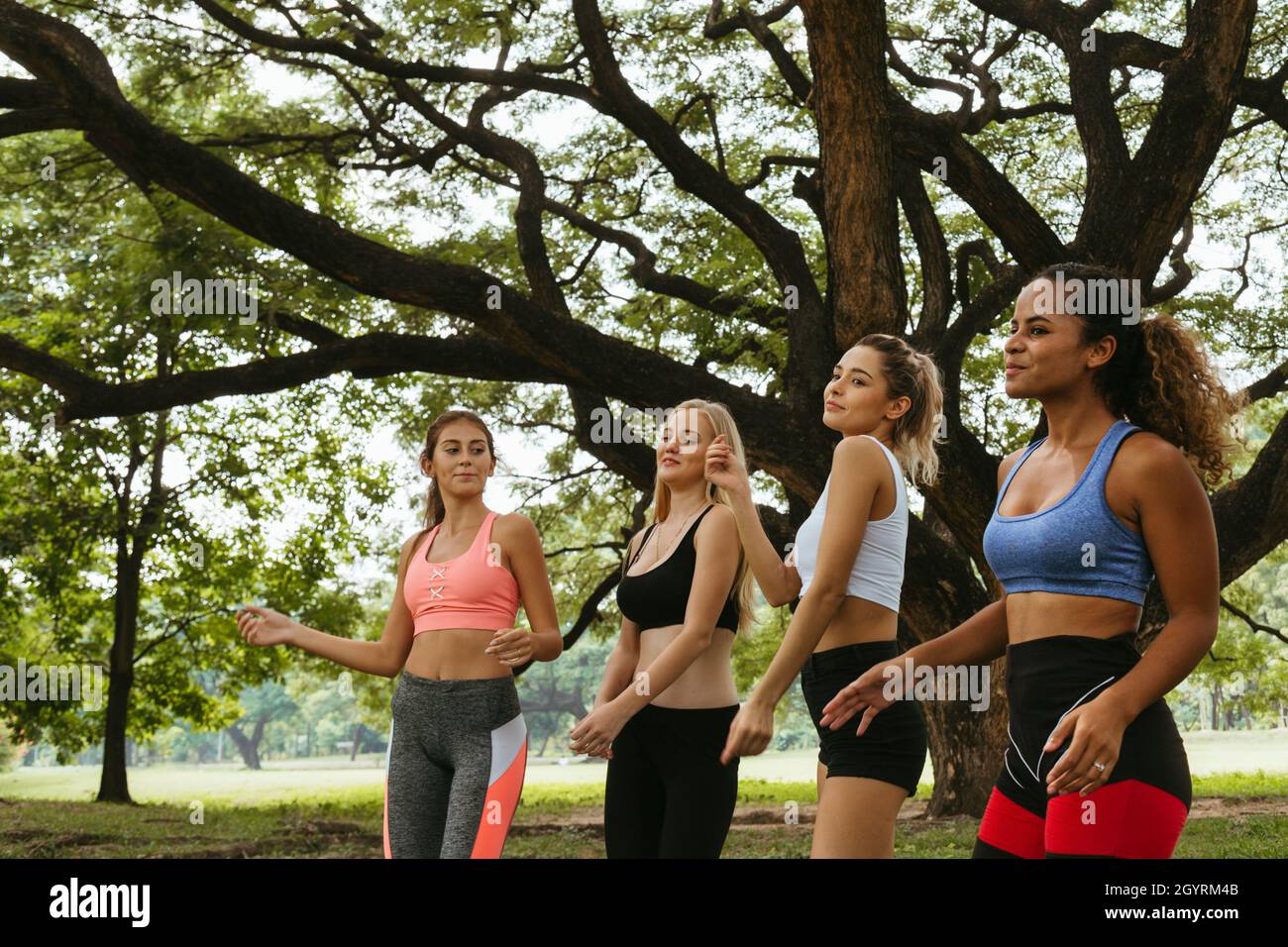 felice giovane multietnica donne adolescenti amici gruppo rilassarsi e ballare dopo l'esercizio nel parco al fine settimana mattina. vita dopo covid. Foto Stock