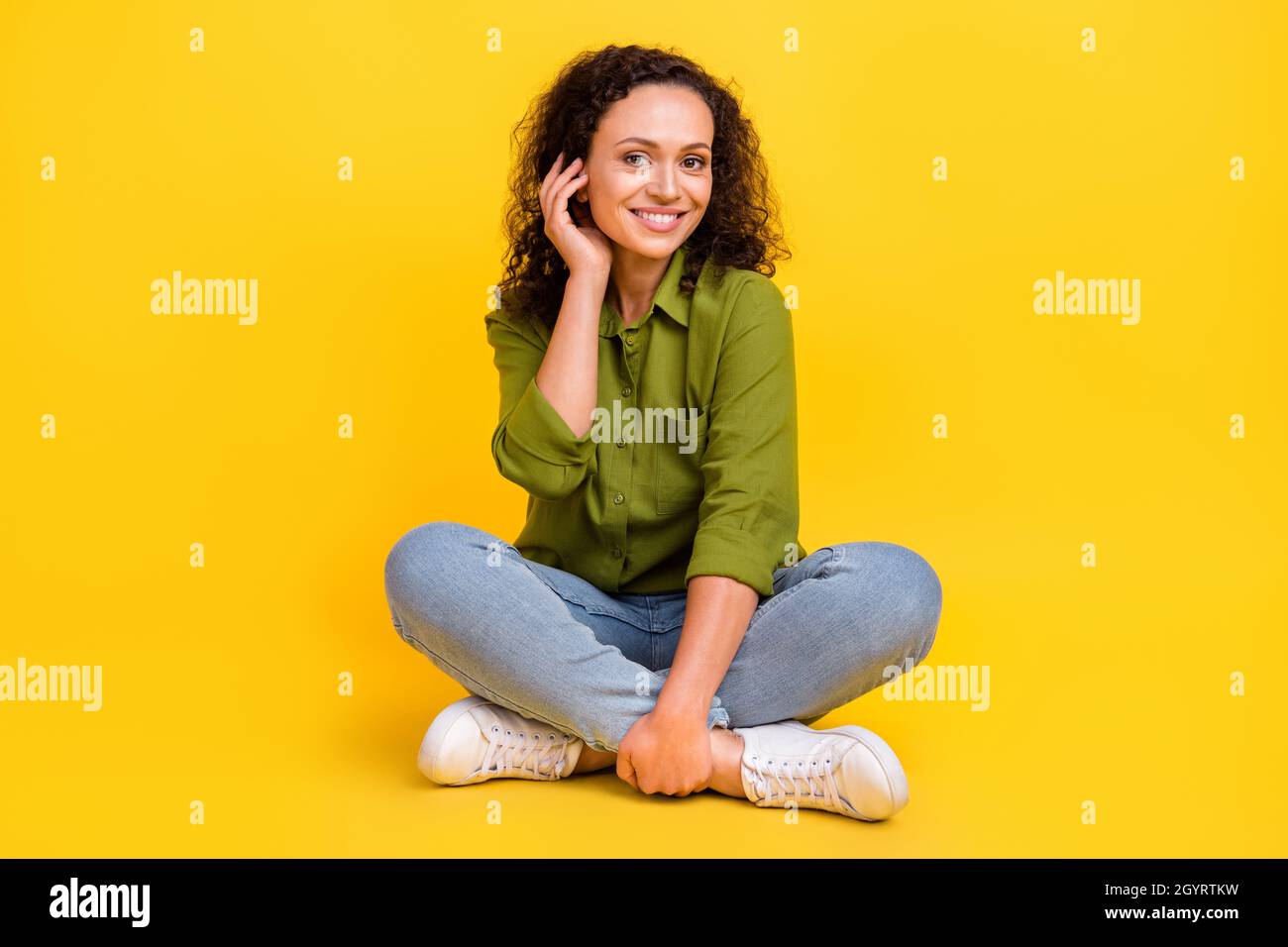 Foto di sognante adorabile donna vestita camicia verde seduta gambe pavimento incrociato braccio hairdo sorridente isolato colore sfondo giallo Foto Stock