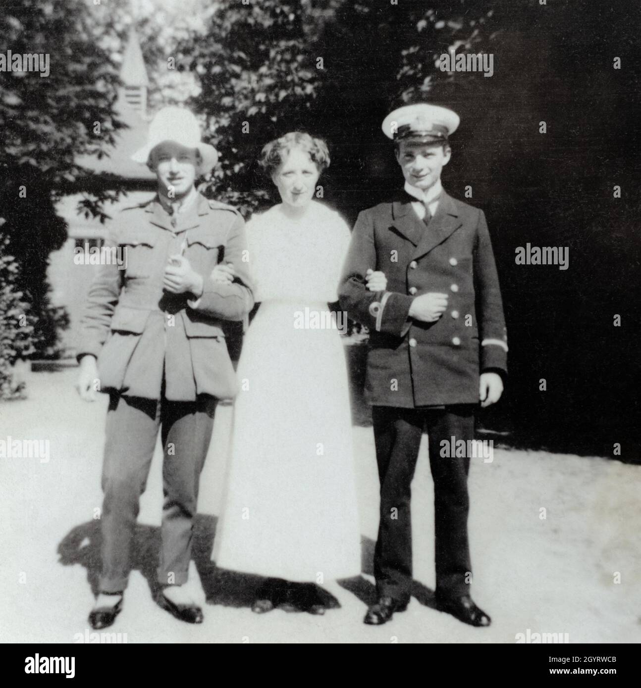 Un ritratto della prima guerra mondiale di una madre che si erige i suoi figli, ufficiali in uniforme. L'uomo a sinistra complimenta la sua divisa ufficiale dell'esercito britannico con quello che sembra essere donna scarpe e cappello. L'uomo a destra ha mantenuto un aspetto più regolamentato nell'uniforme di un sub-tenente nella Royal Navy. Foto Stock