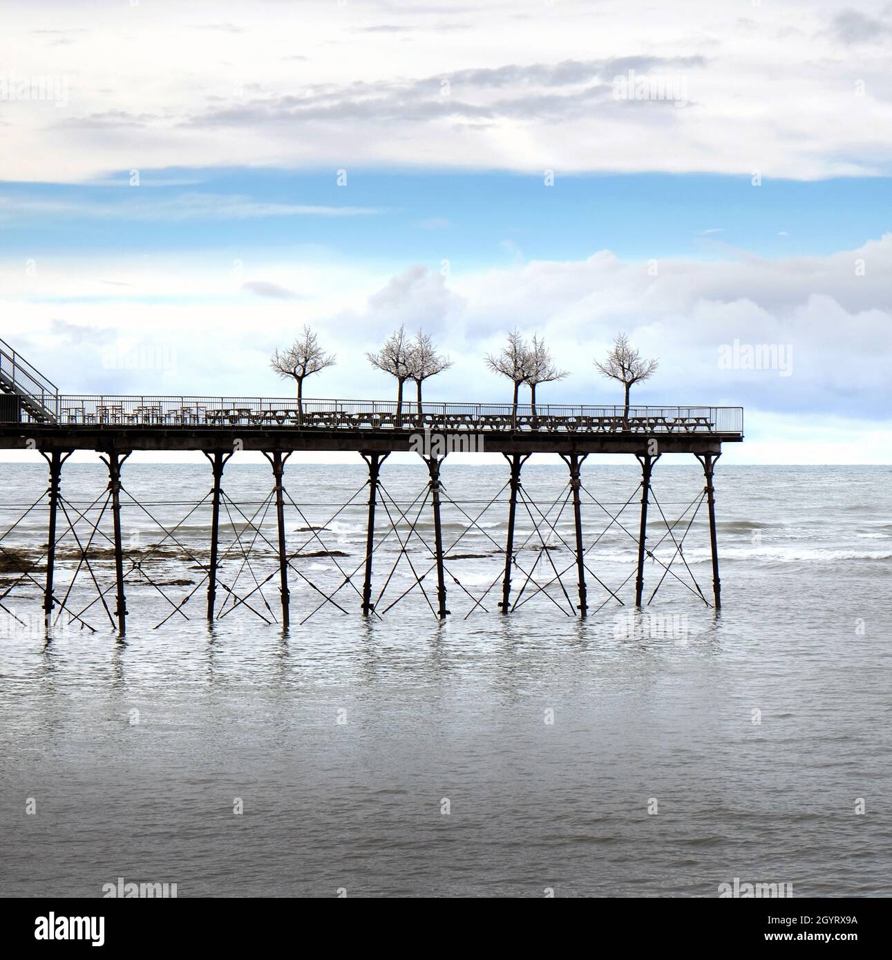 Royal Pier, Aberystwyth, Galles, Regno Unito. Alberi decorativi imitazione delineati alla fine del molo. Cielo blu con le nuvole sopra e mare calmo sotto Foto Stock