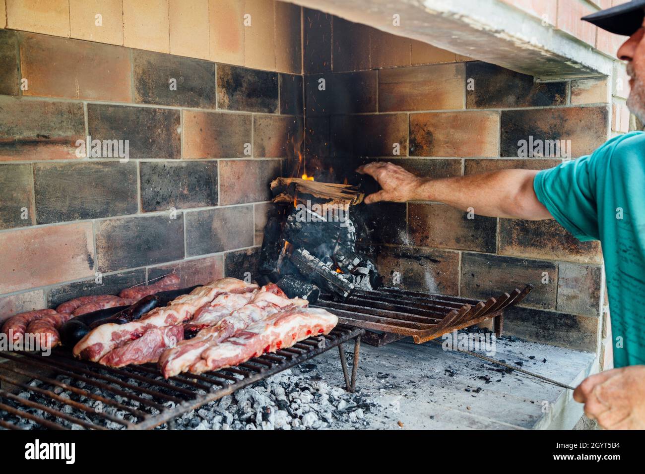Uomo maturo che fa un barbecue. Sta aggiungendo legna al fuoco. Foto Stock