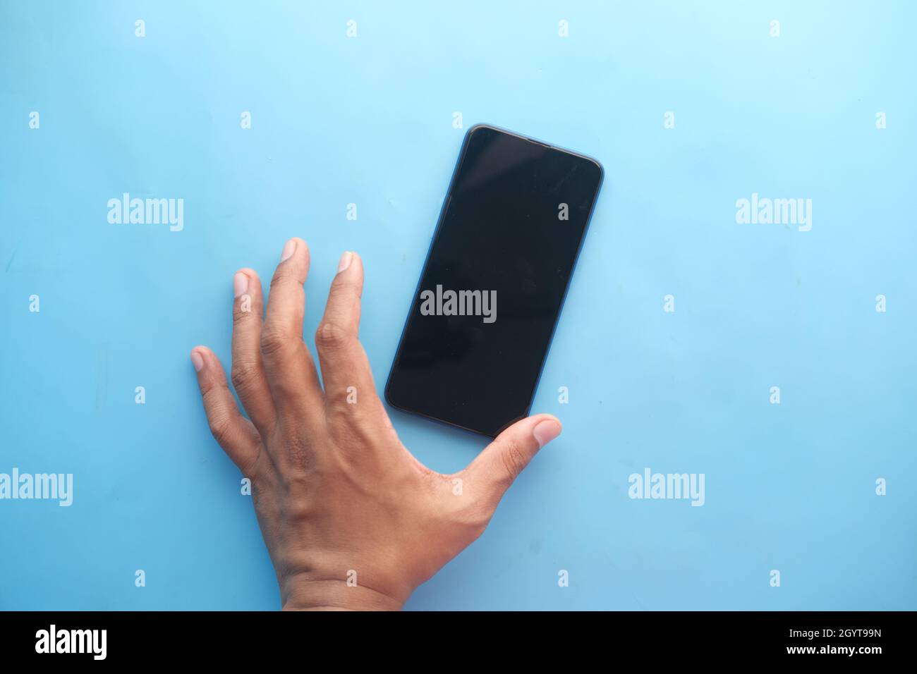 Primo piano della mano del giovane uomo che tiene uno smartphone su blu Foto Stock