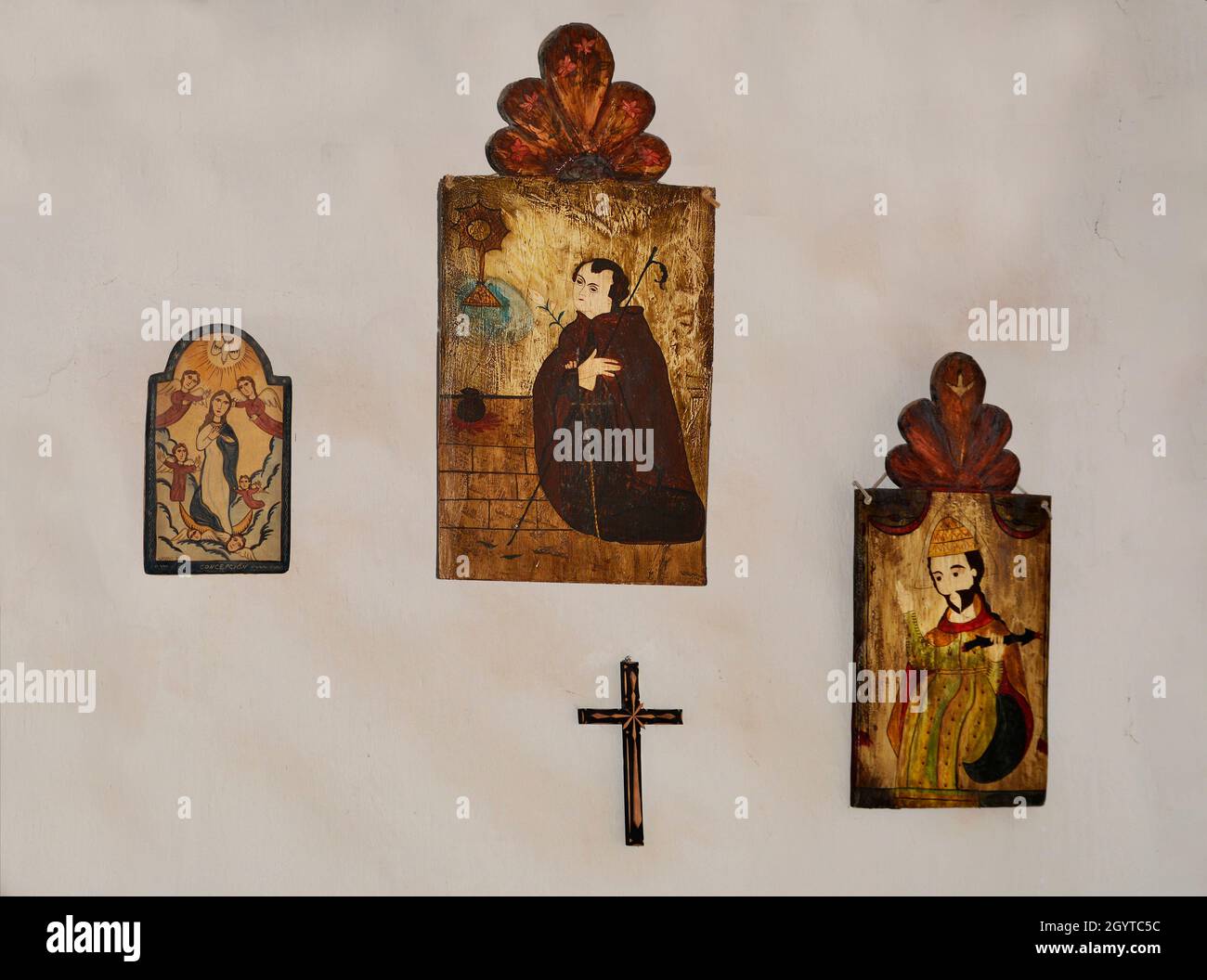 Tabli in legno e un crocifisso appendere sul muro di una storica casa in adobe al complesso di storia vivente El Rancho de las Golondrinas vicino a Santa Fe, NM. Foto Stock